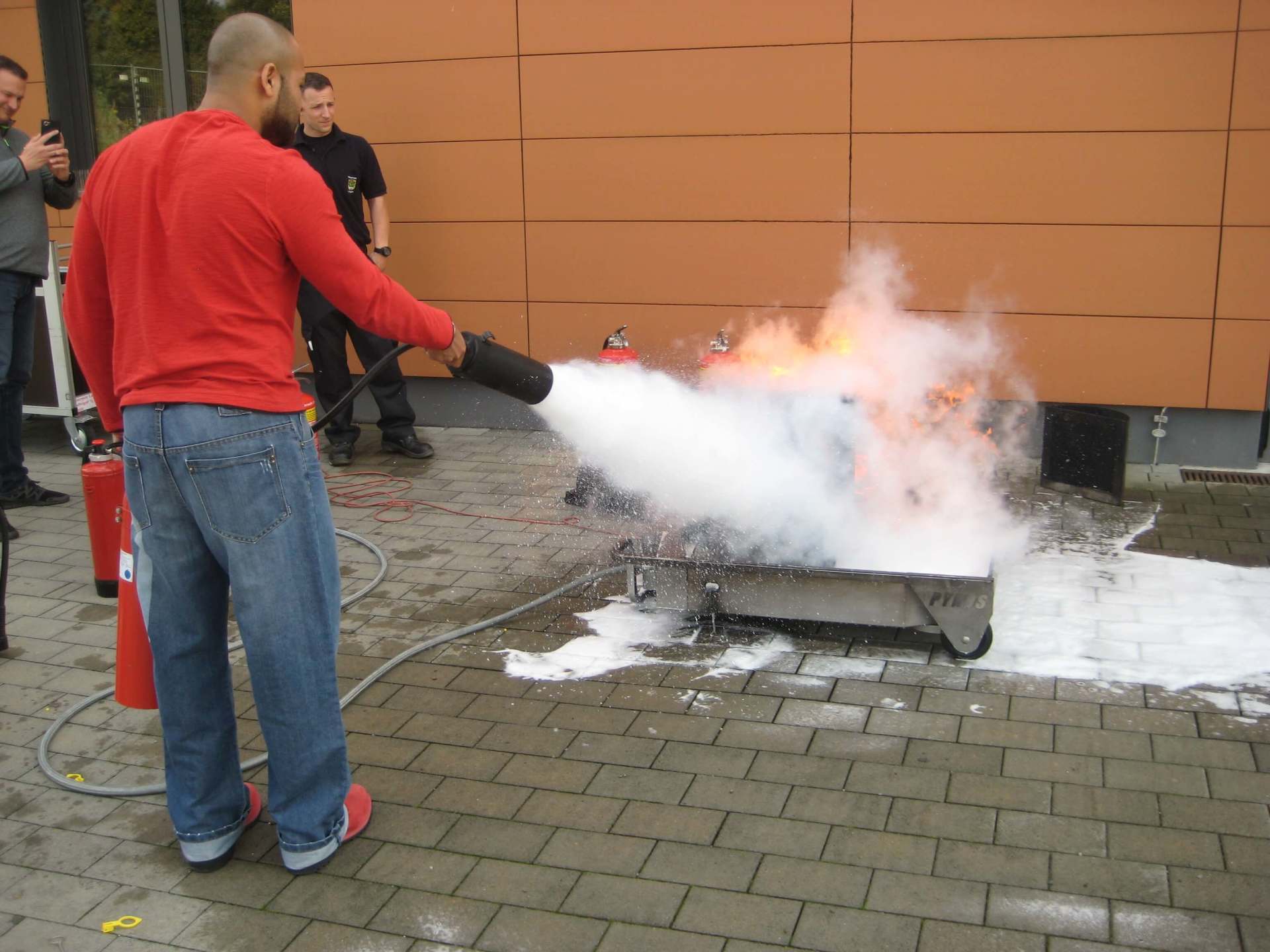 Ein Mann in einem roten Hemd benutzt einen Feuerlöscher, um ein Feuer zu löschen