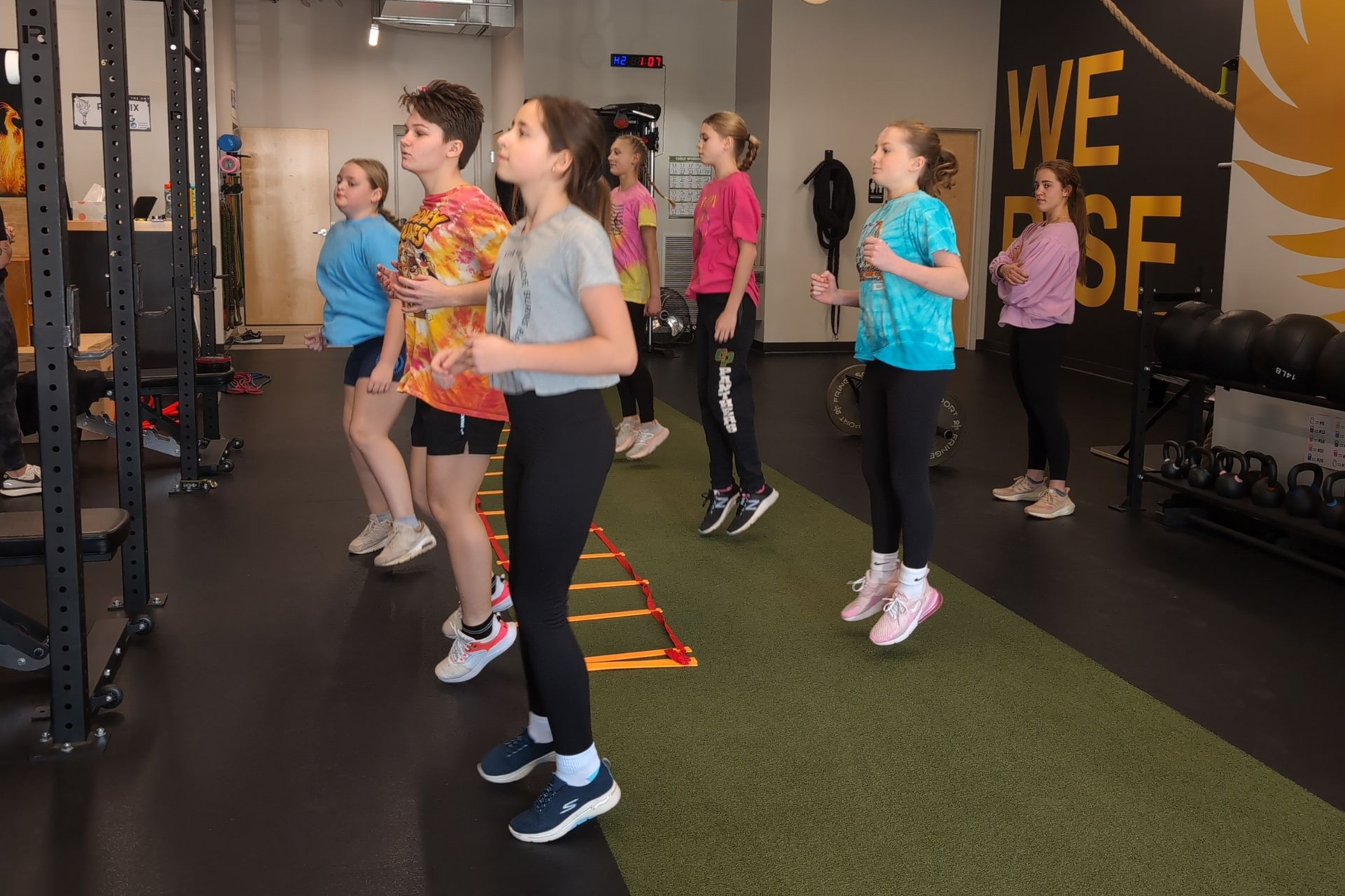 Two women in a kitchen, one in yellow jacket and one in a light dress, are talking at a counter with papers.
