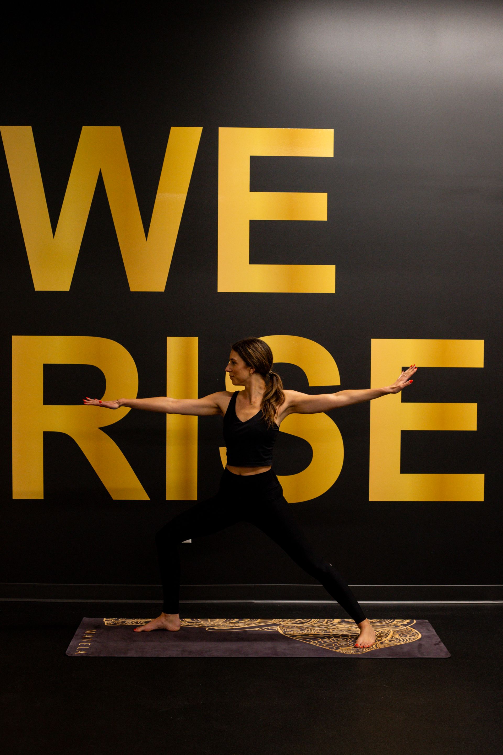 Woman in yoga pose in front of a black wall with gold 