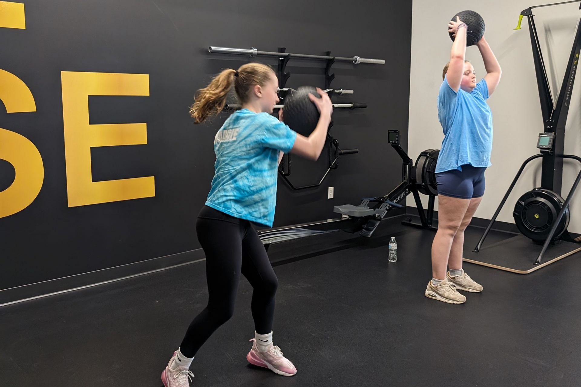 Two women in a kitchen, one in yellow jacket and one in a light dress, are talking at a counter with papers.