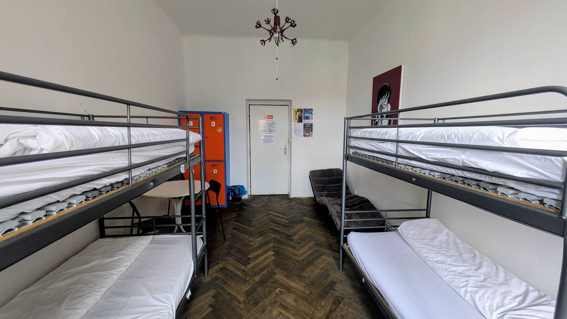 Hostel dorm room with two sets of bunk beds, lockers, and a door.