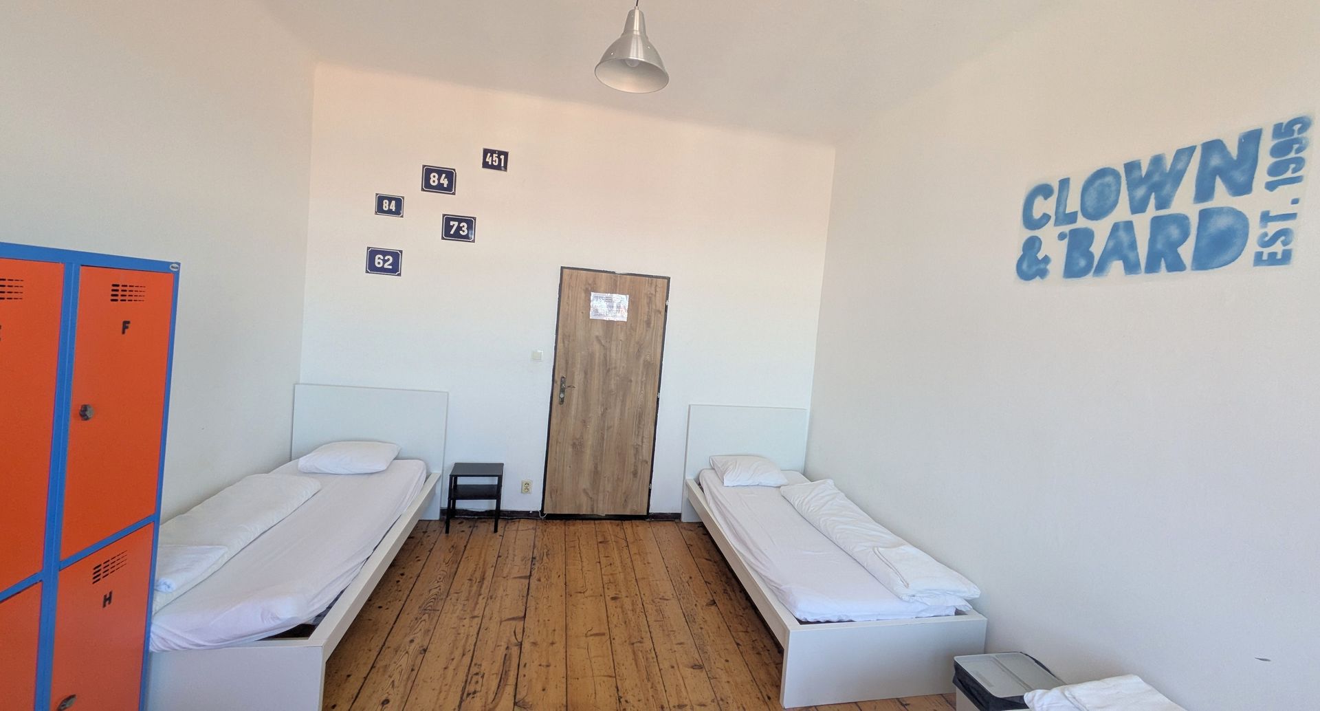 A bright room with two beds, lockers, and a door. 