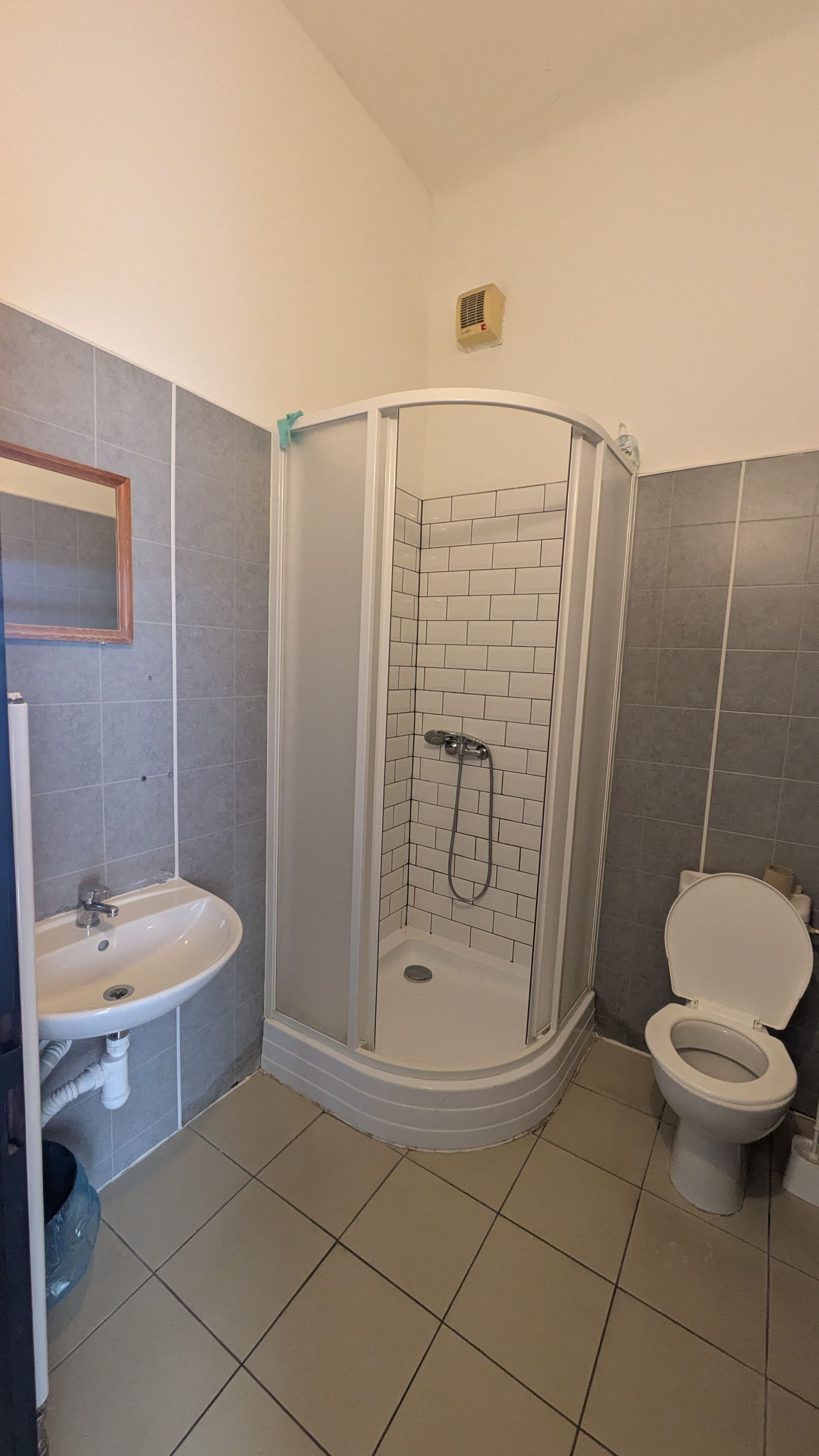 Bathroom with shower, toilet, and sink. Walls are tiled grey and white.