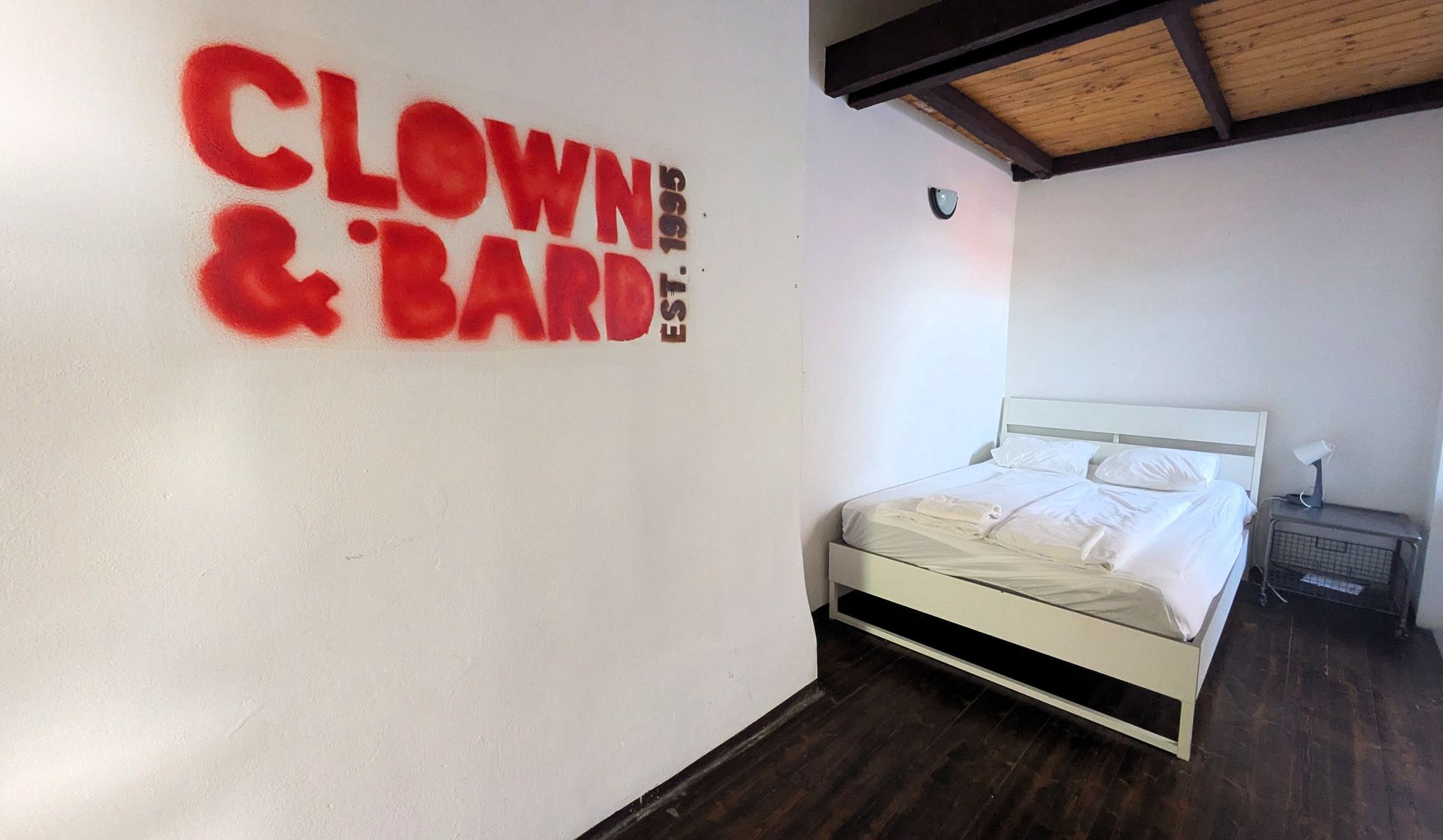 Bedroom with white walls, a bed, and the red logo 