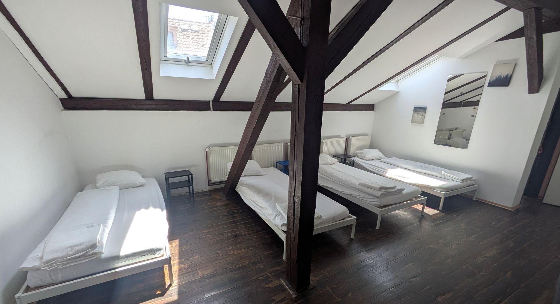 Attic room with four single beds, wooden beams, and a skylight.