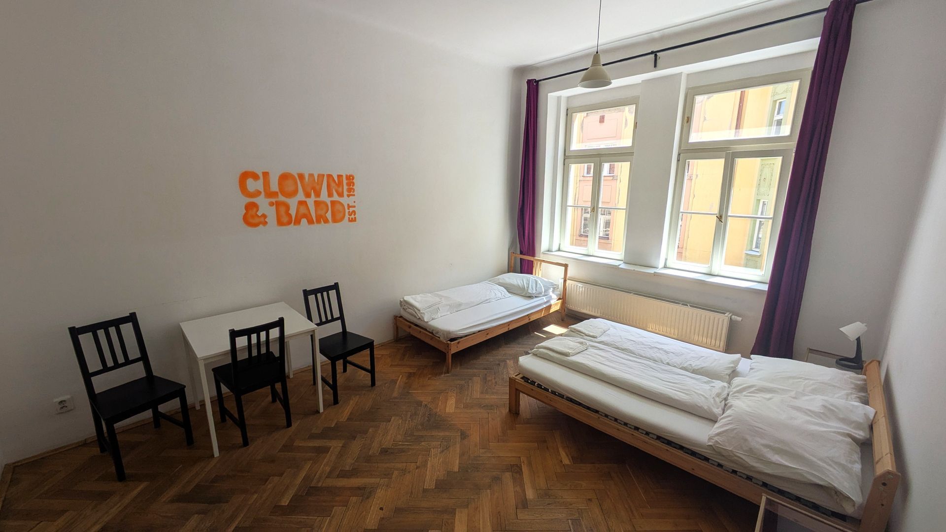 Bedroom with two beds, a table, and chairs. Orange text on wall reads 