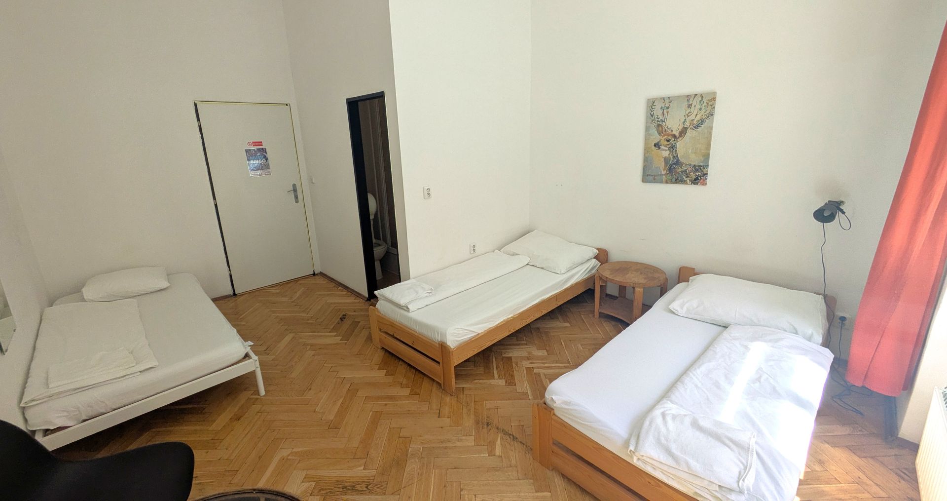 A room with three single beds, a door, and a small nightstand.