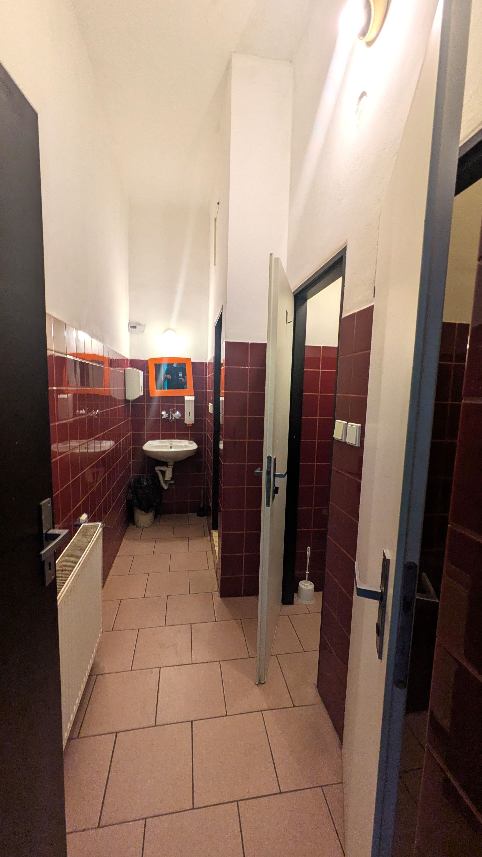 Hallway with red tiled walls, doorways to the bathroom and showers, and a sink.