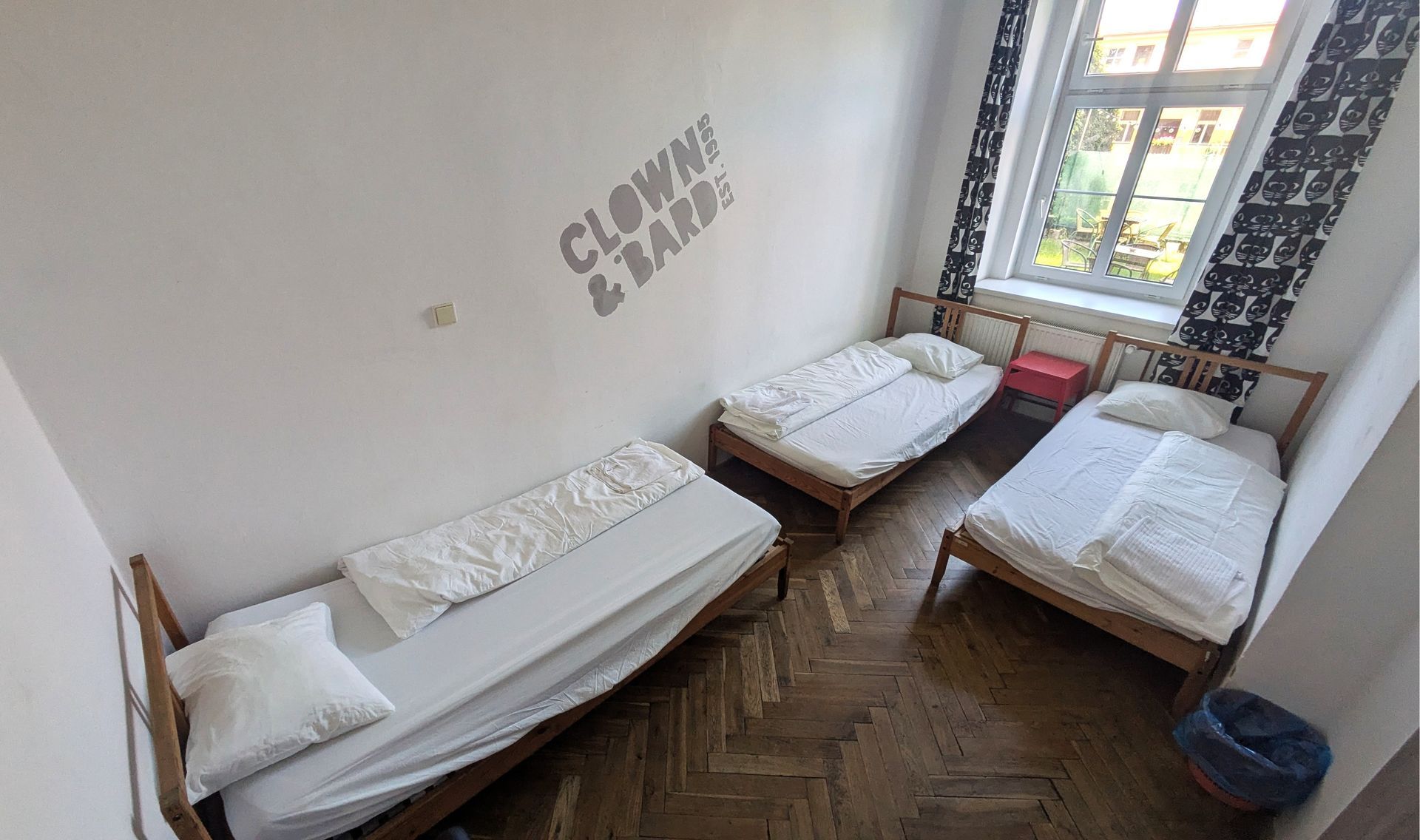 Three single beds in a room with white walls, a window, and wooden floors.
