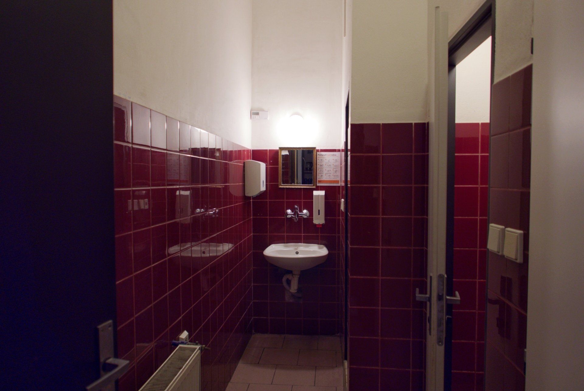 Small bathroom with red tile walls, white ceiling, sink, and open doorway.