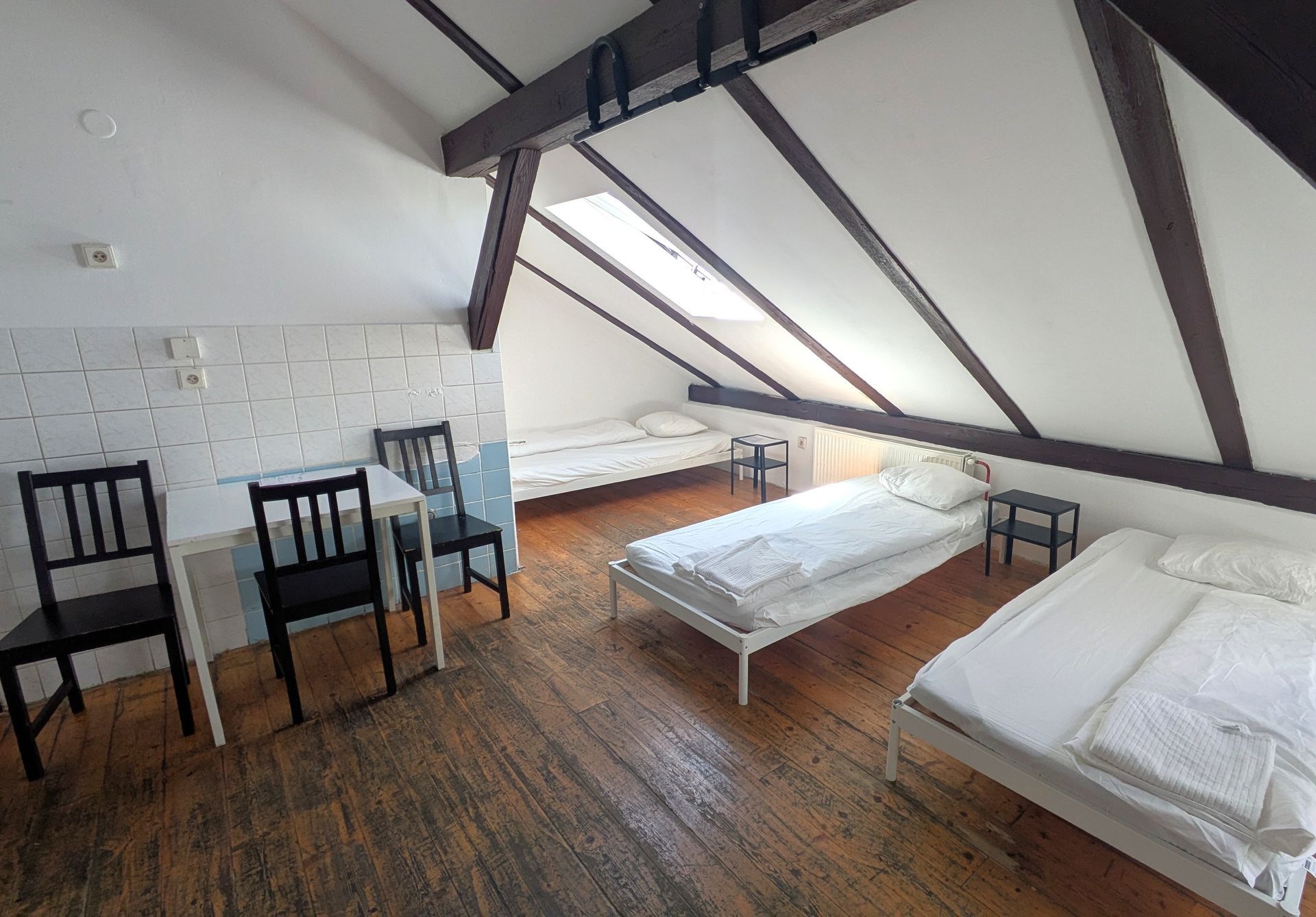 Attic room with wood floors, white beds, and table with chairs. Exposed beams and slanted ceiling.