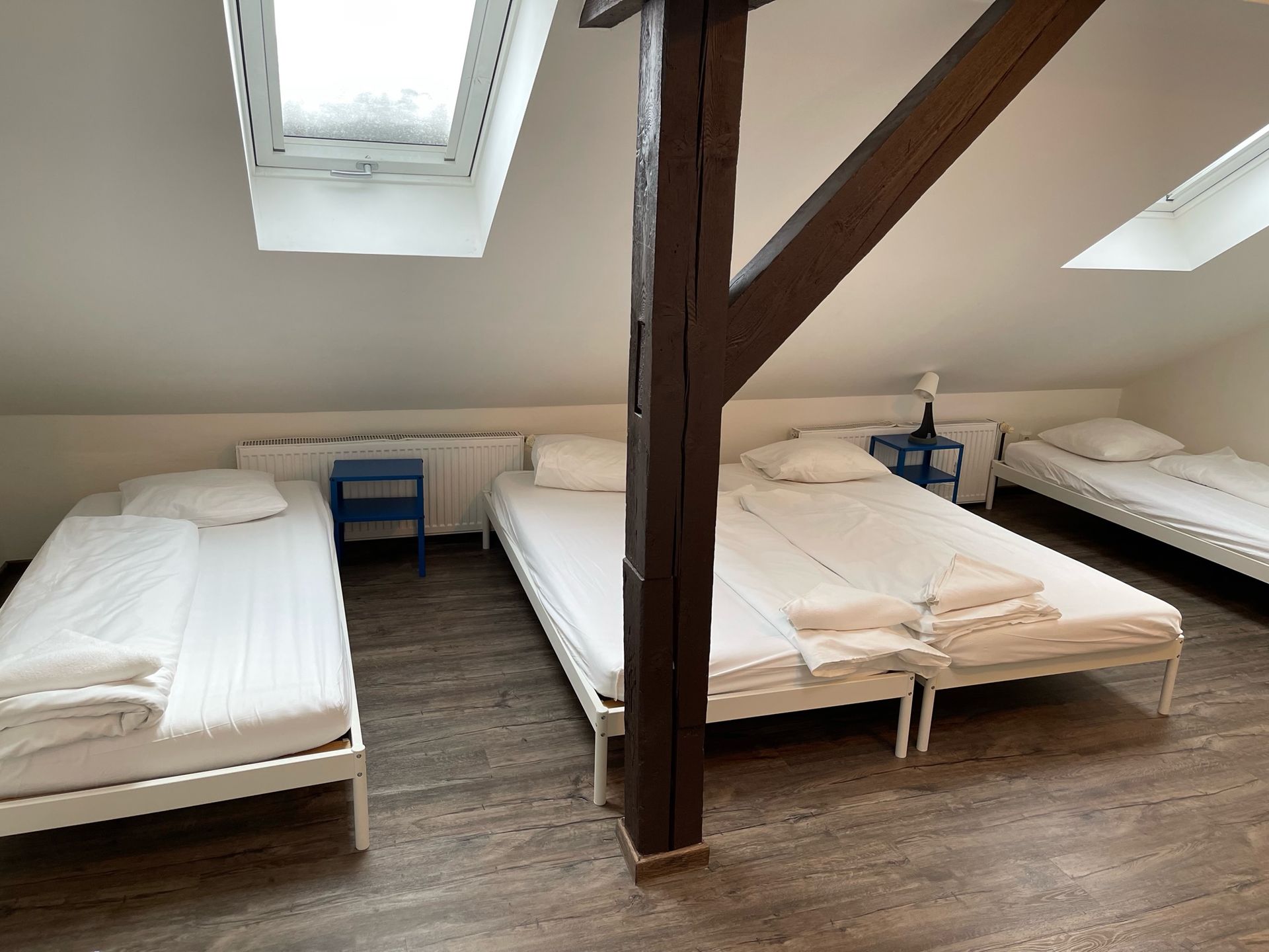 Attic room with three beds, a wooden beam, and two skylights. Beds are white with white bedding.