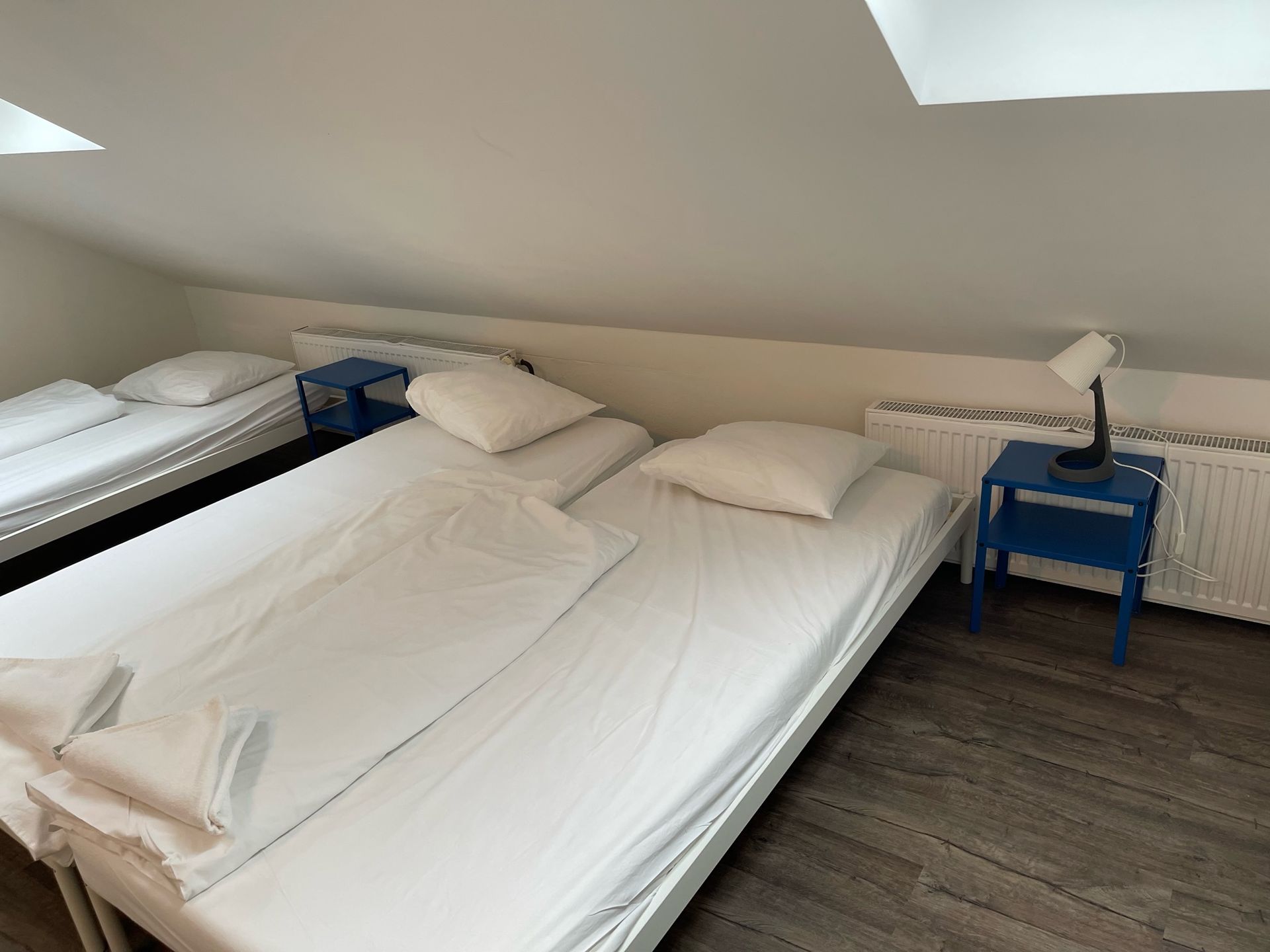 Bedroom with three beds, white sheets, blue nightstands, and a desk lamp.