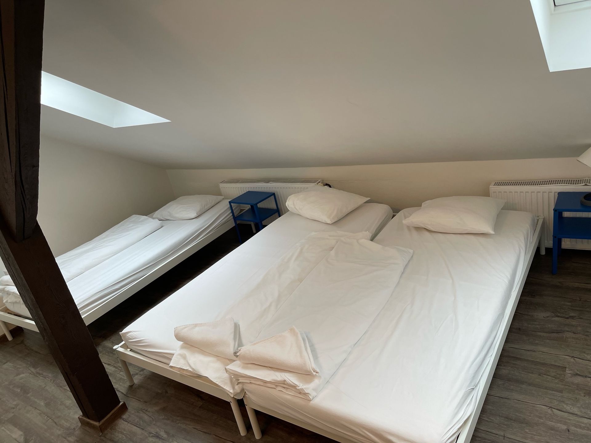 Bedroom with three beds under a sloped ceiling. Two beds are side-by-side, one is separate. Blue nightstands.