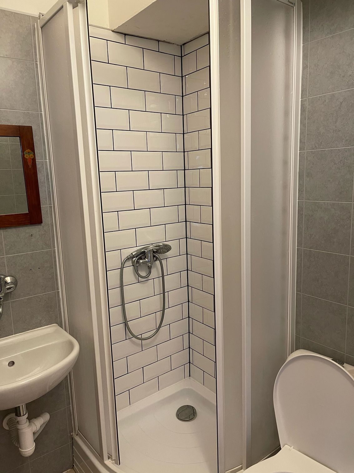 Bathroom with shower stall, toilet, and sink. White subway tile in shower, gray walls.