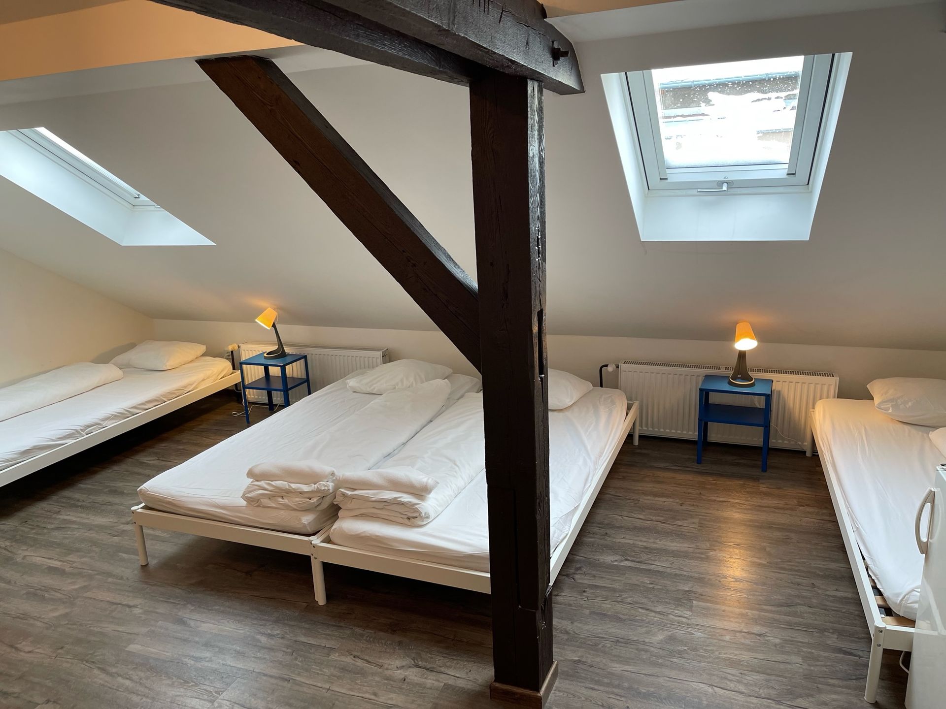 Attic bedroom with three beds, a dark support beam, and two skylight windows.