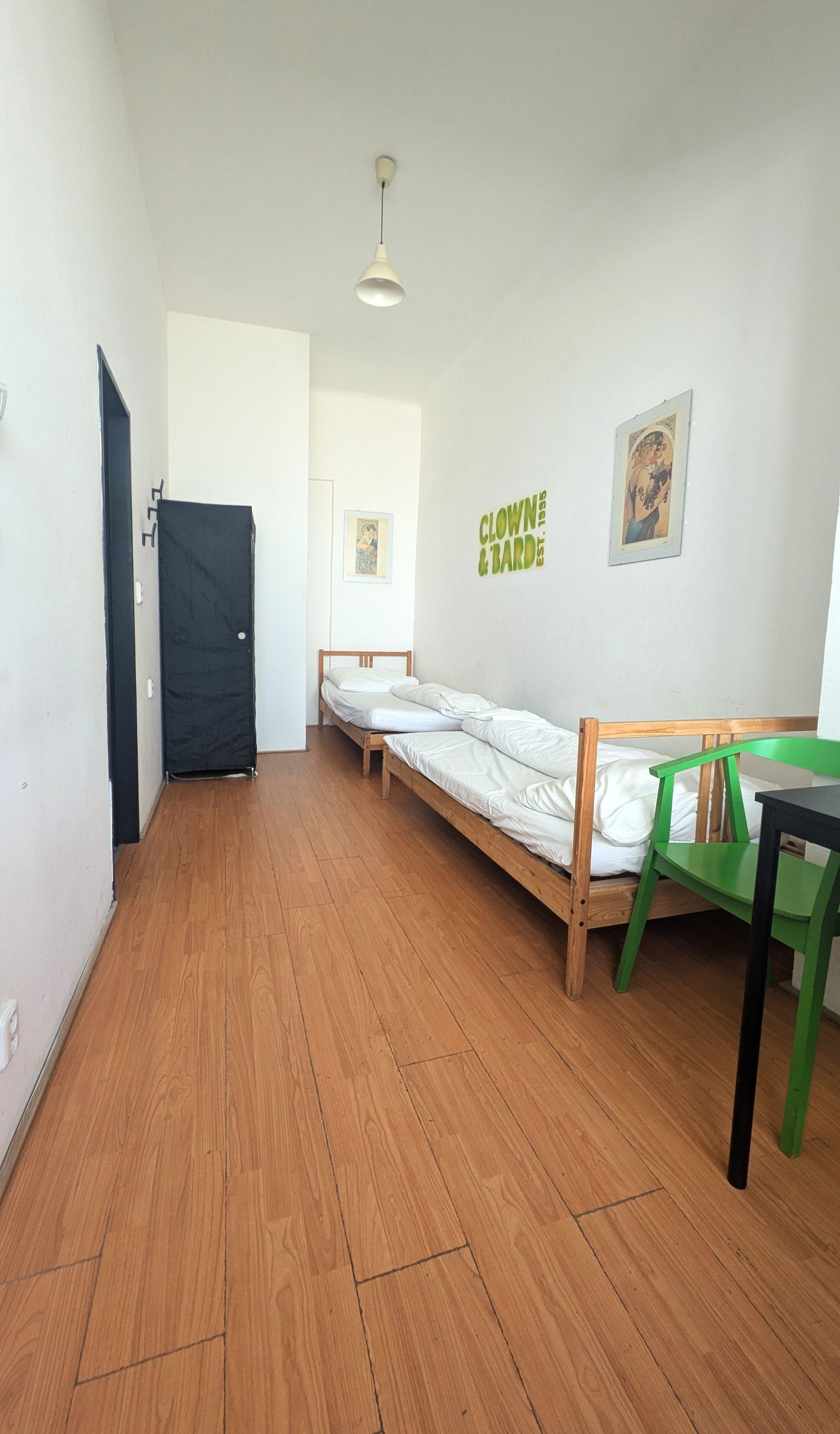 A room with a bed, green chair, dark closet, and wooden floor. Bright overhead light.