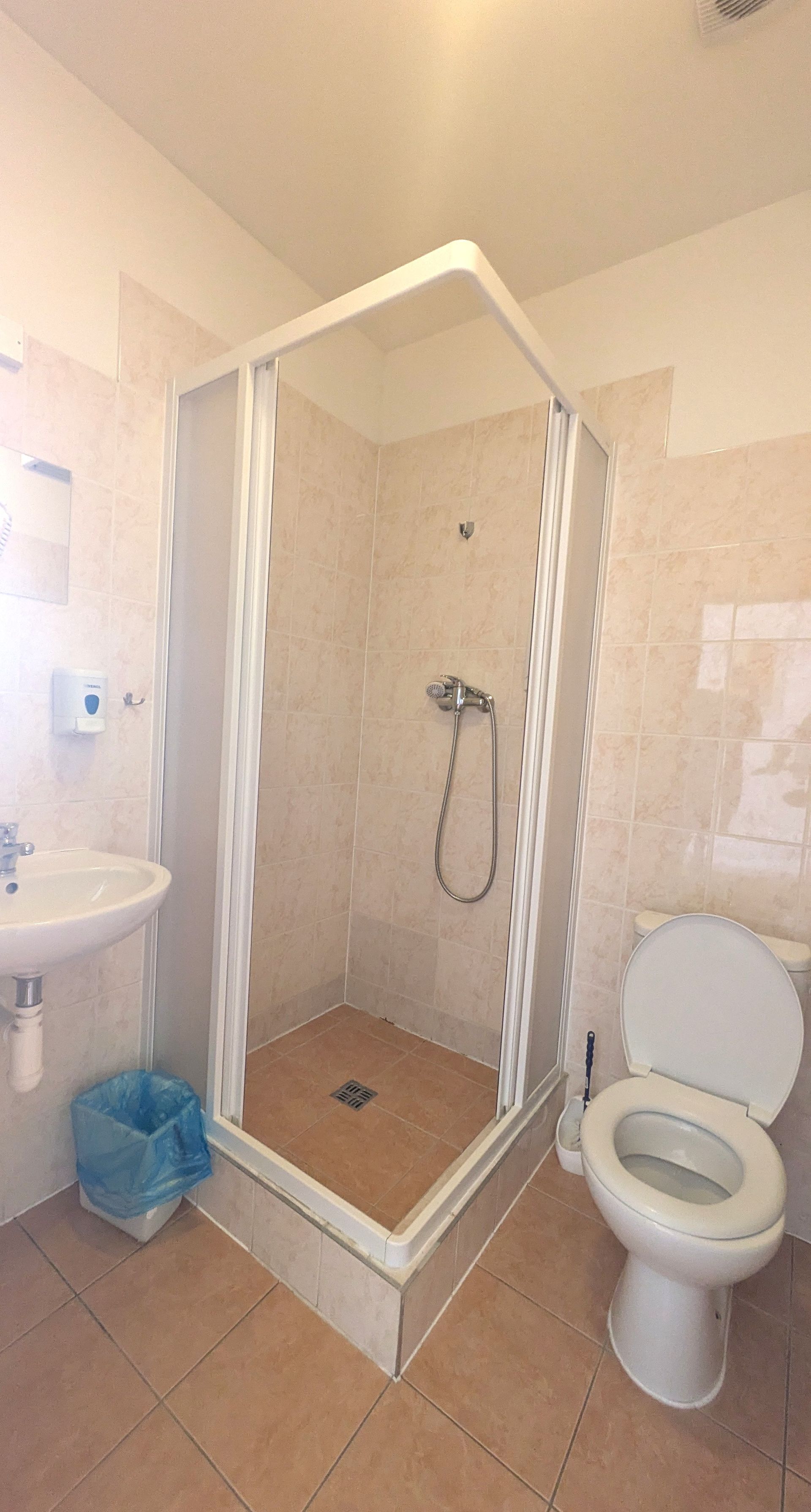 Bathroom with a shower, toilet, and sink; beige tiled walls.