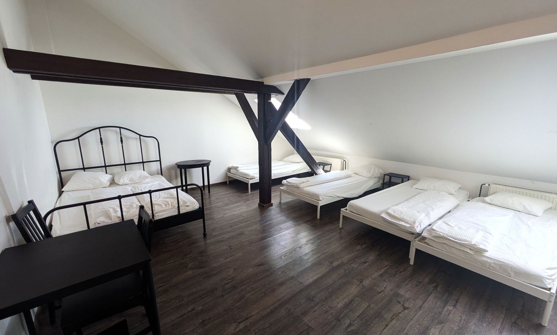 Bedroom with multiple beds under a sloped ceiling; wood floors and dark wooden beams.