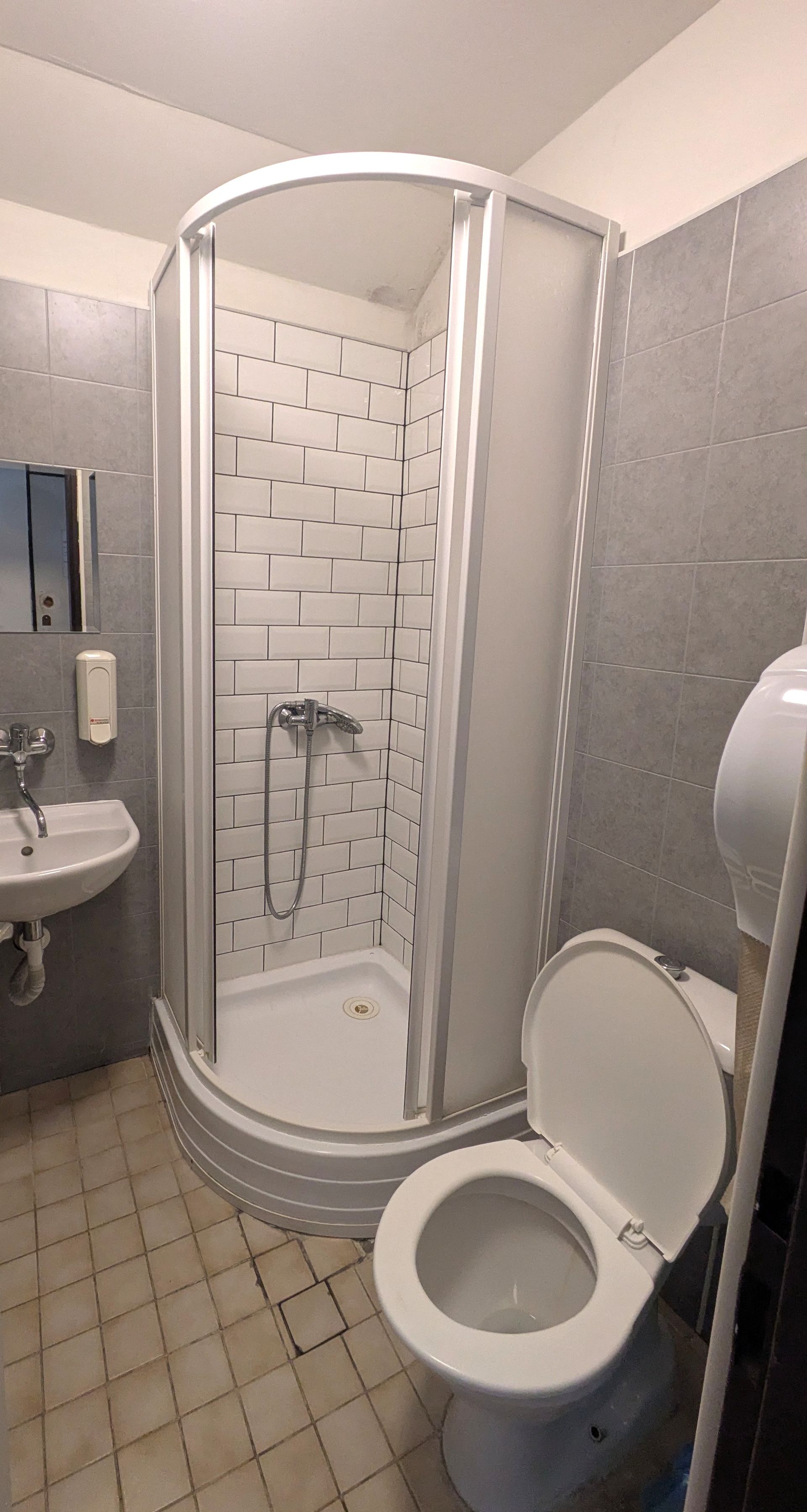 Bathroom with shower stall, toilet, sink, and tiled walls.