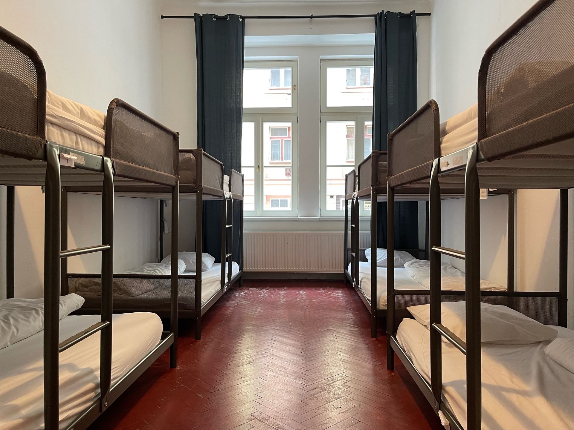 Hostel dorm room with multiple bunk beds, window, and red floor.