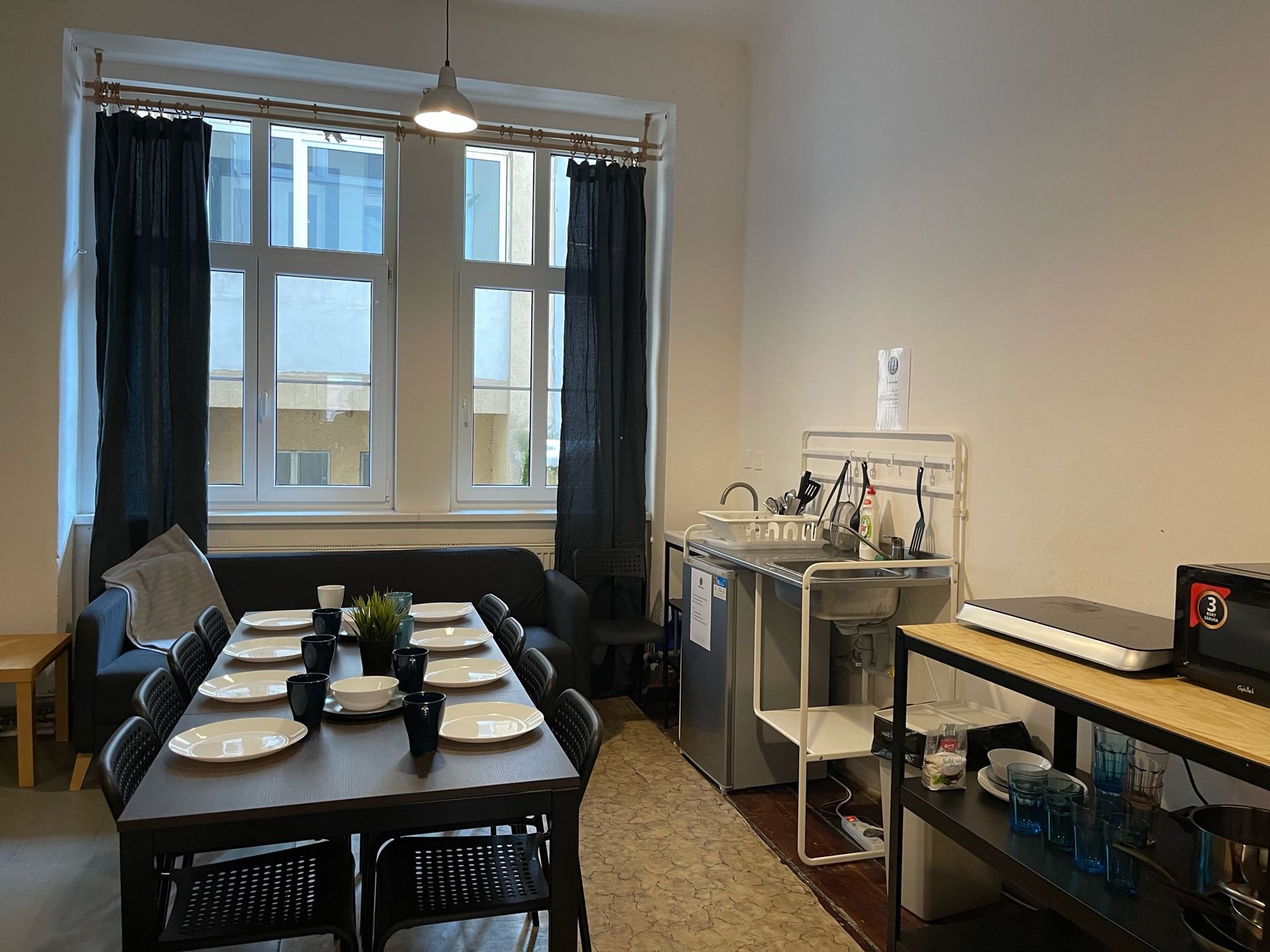 Dining area with table set for many, near a window, and a small kitchen area.