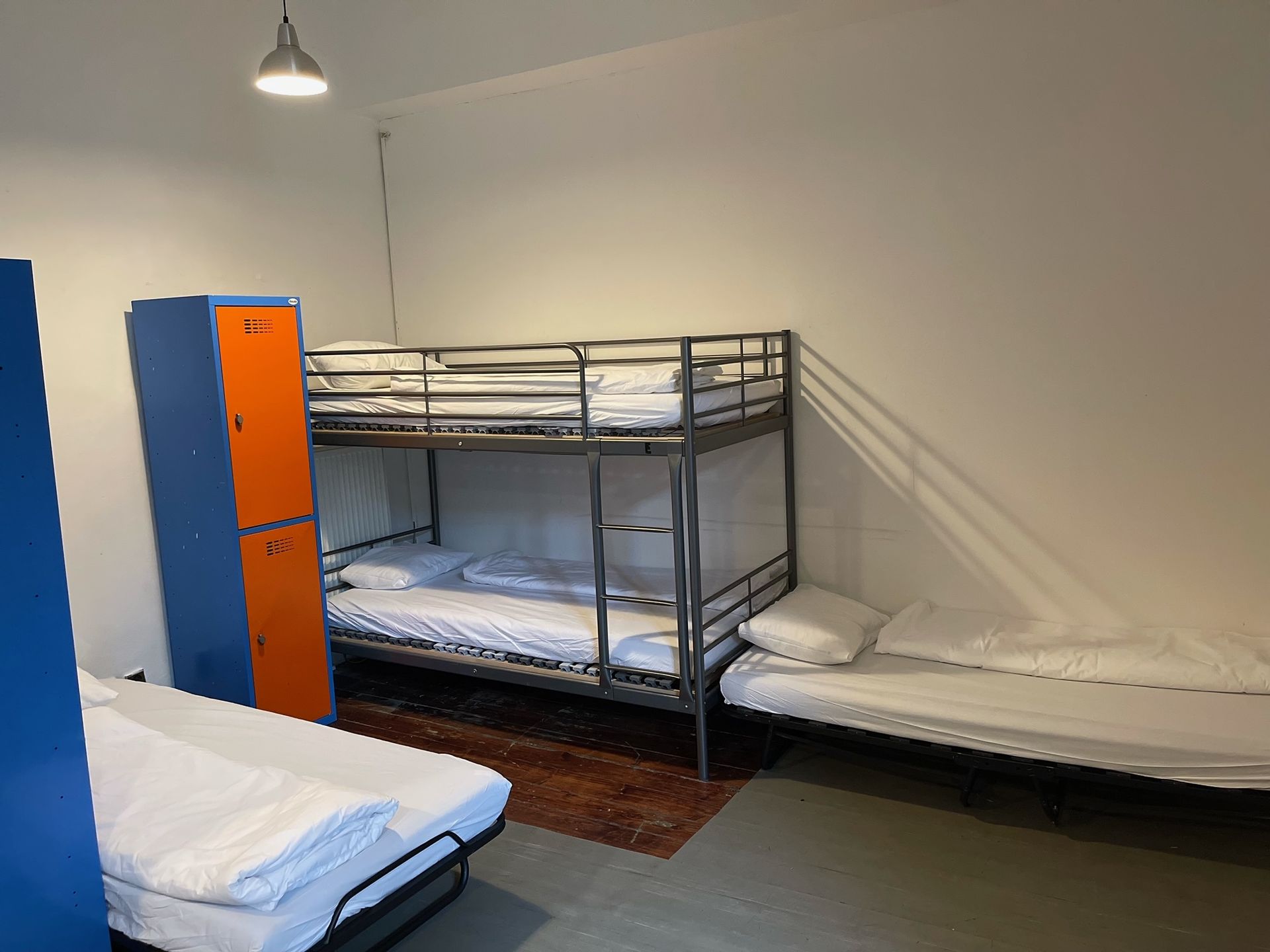 Bunk bed and two single beds in a hostel room with lockers and a light fixture.