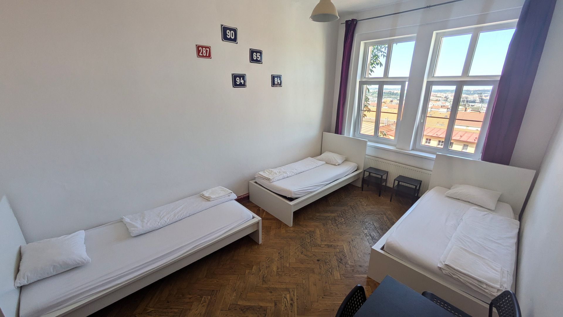 Three single beds in a bright room with a large window and purple curtains.
