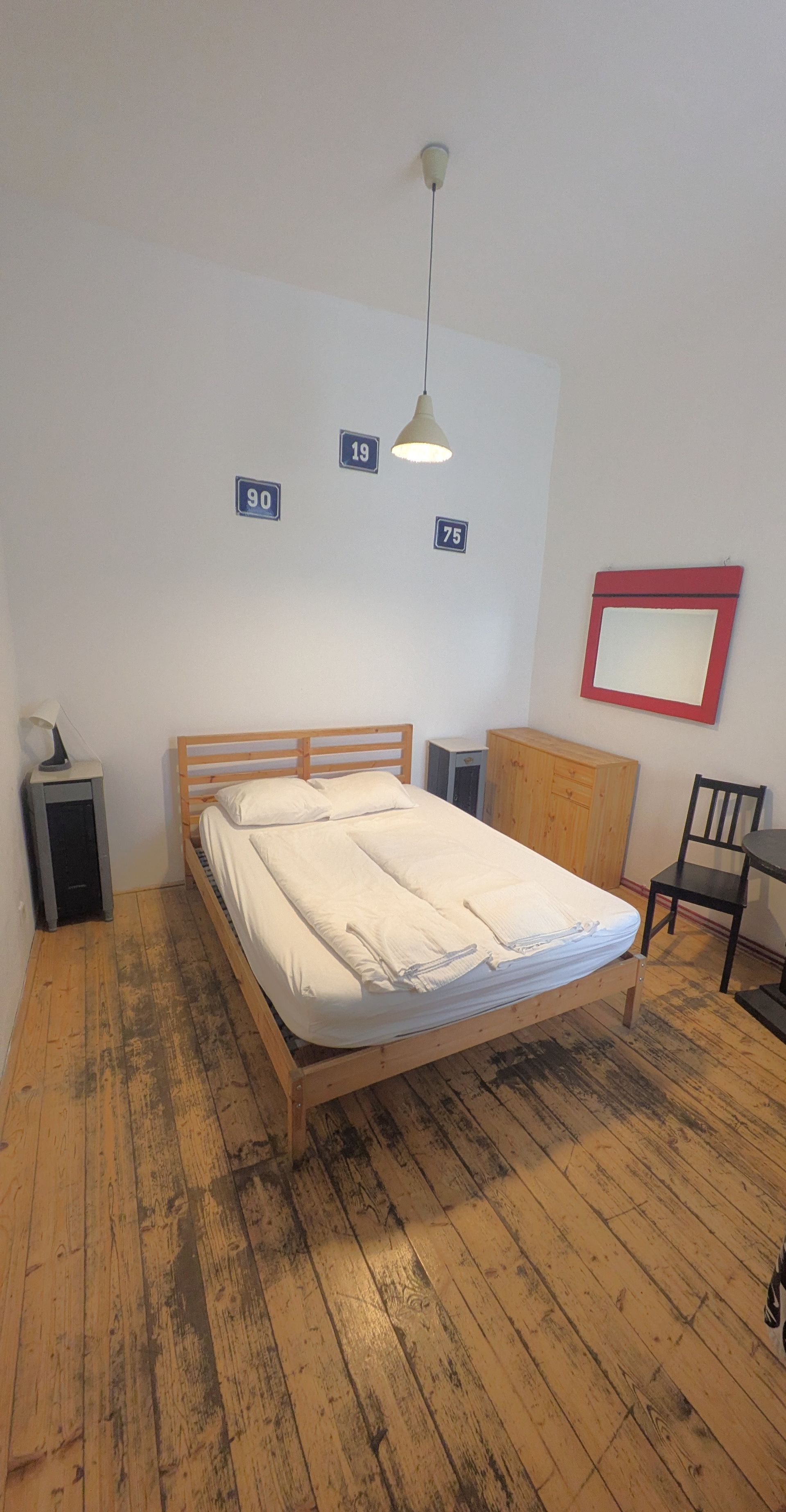 Bedroom with bed, dresser, mirror, and hardwood floors. White walls and a hanging light.