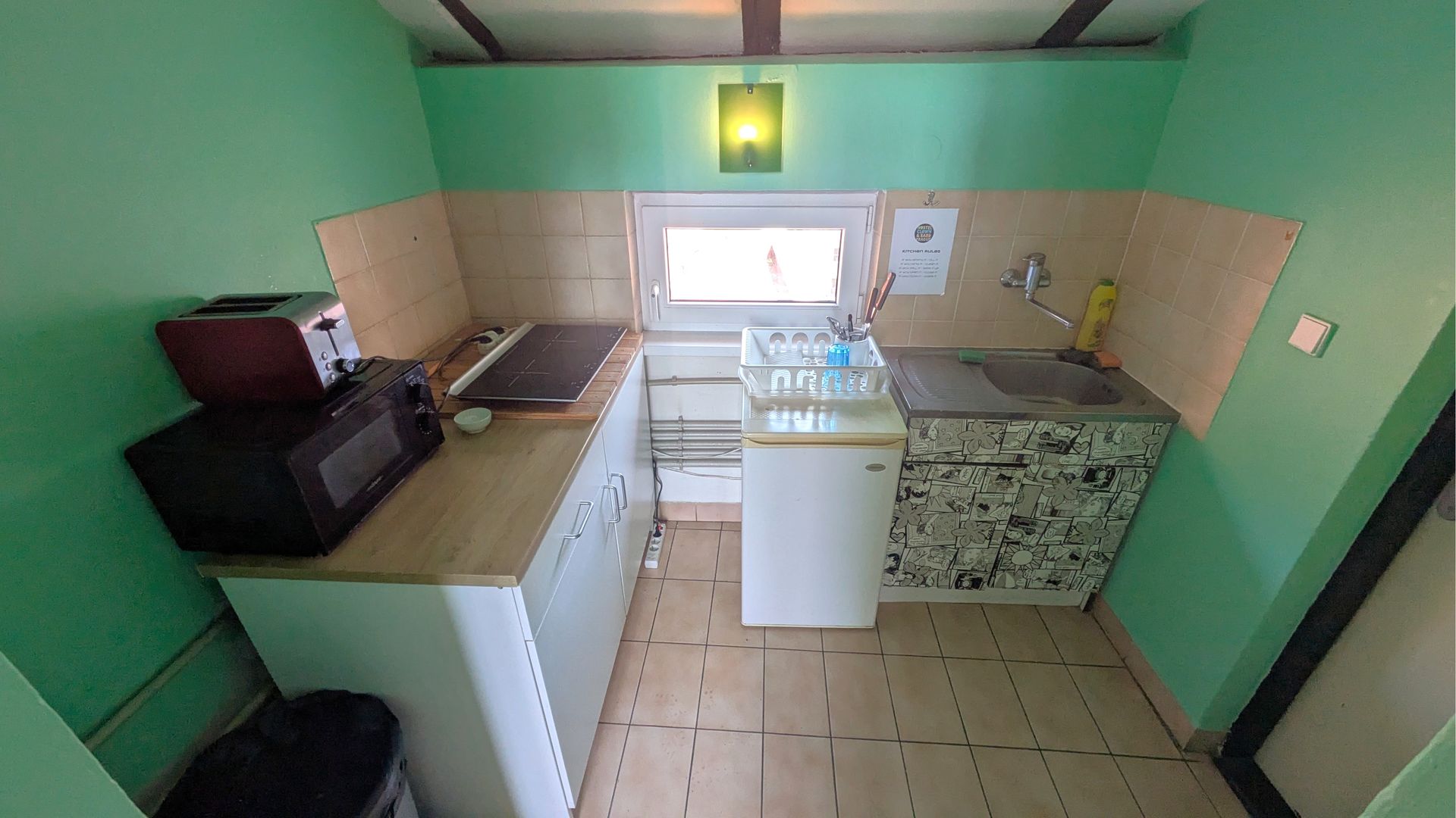 Small kitchen with white cabinets, appliances, light green walls, and a small window.