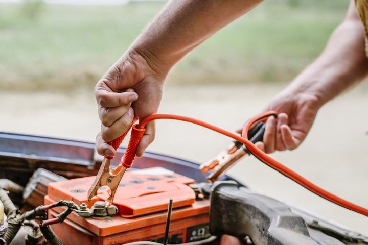 Person connecting jumper cables to a car battery in an outdoor setting.
