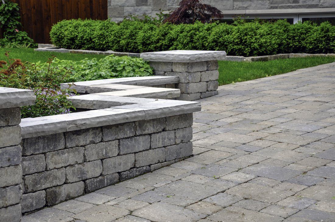 A brick walkway with a stone wall and benches in front of a house.