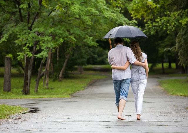 Couple walking barefoot under an umbrella on a wet path in a park.