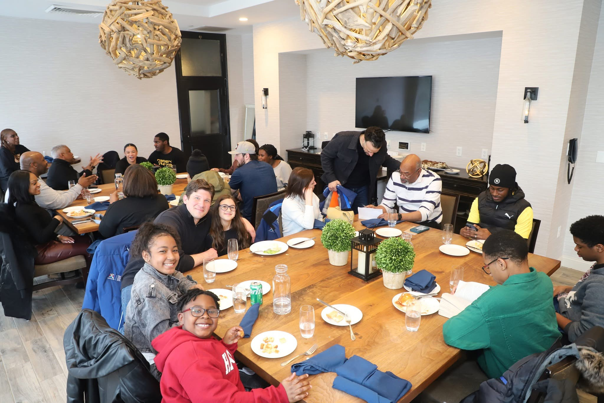 Large group at a restaurant table. People eating, smiling. Modern decor with woven light fixtures.