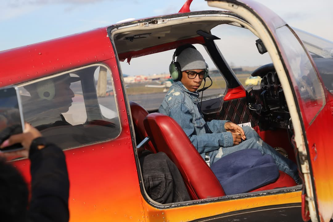 Young person in a red plane cockpit, wearing headset, looking at the camera.