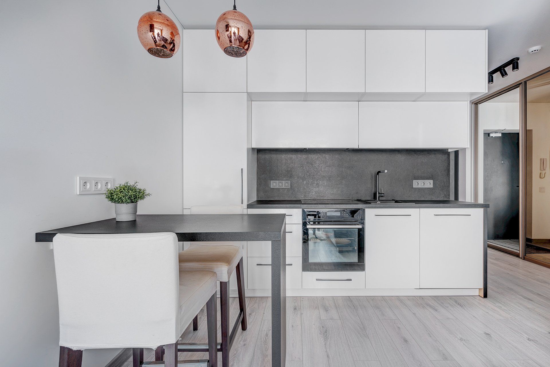 Virtuvė su baltomis spintelėmis, stalu ir kėdėmis.