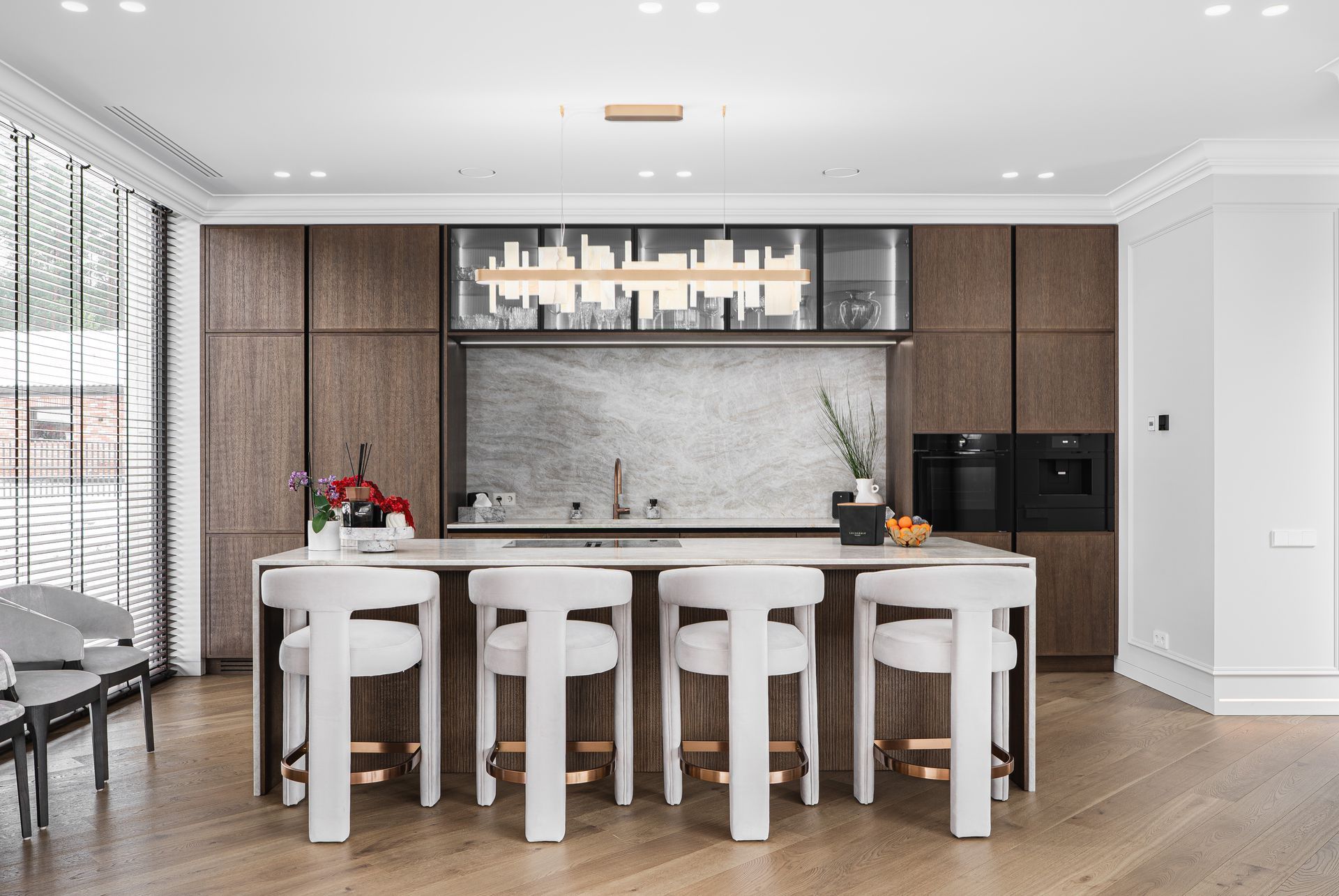Modern kitchen with island, brown cabinetry, white stools, and light fixture.