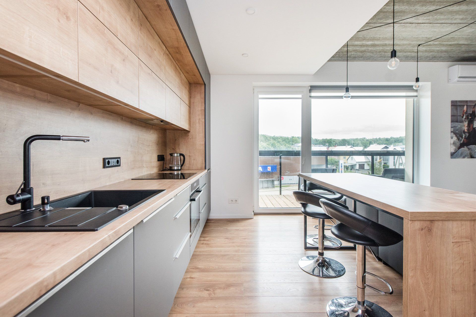 Virtuvė su medinėmis spintelėmis, kriaukle, stalu ir taburetėmis.