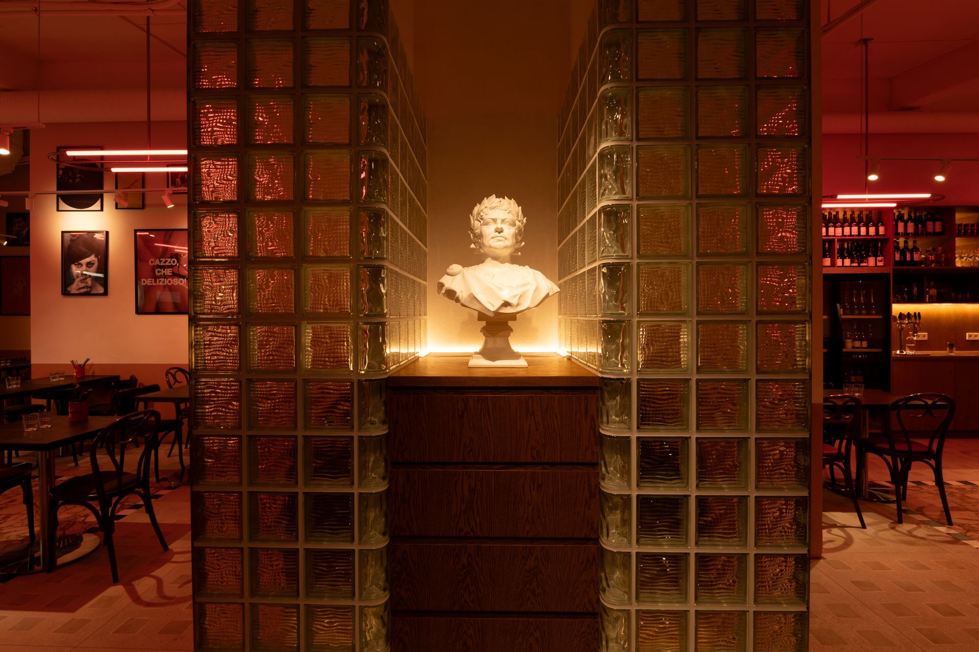 Bust sculpture framed by glass block walls in a dimly lit, red-toned interior.