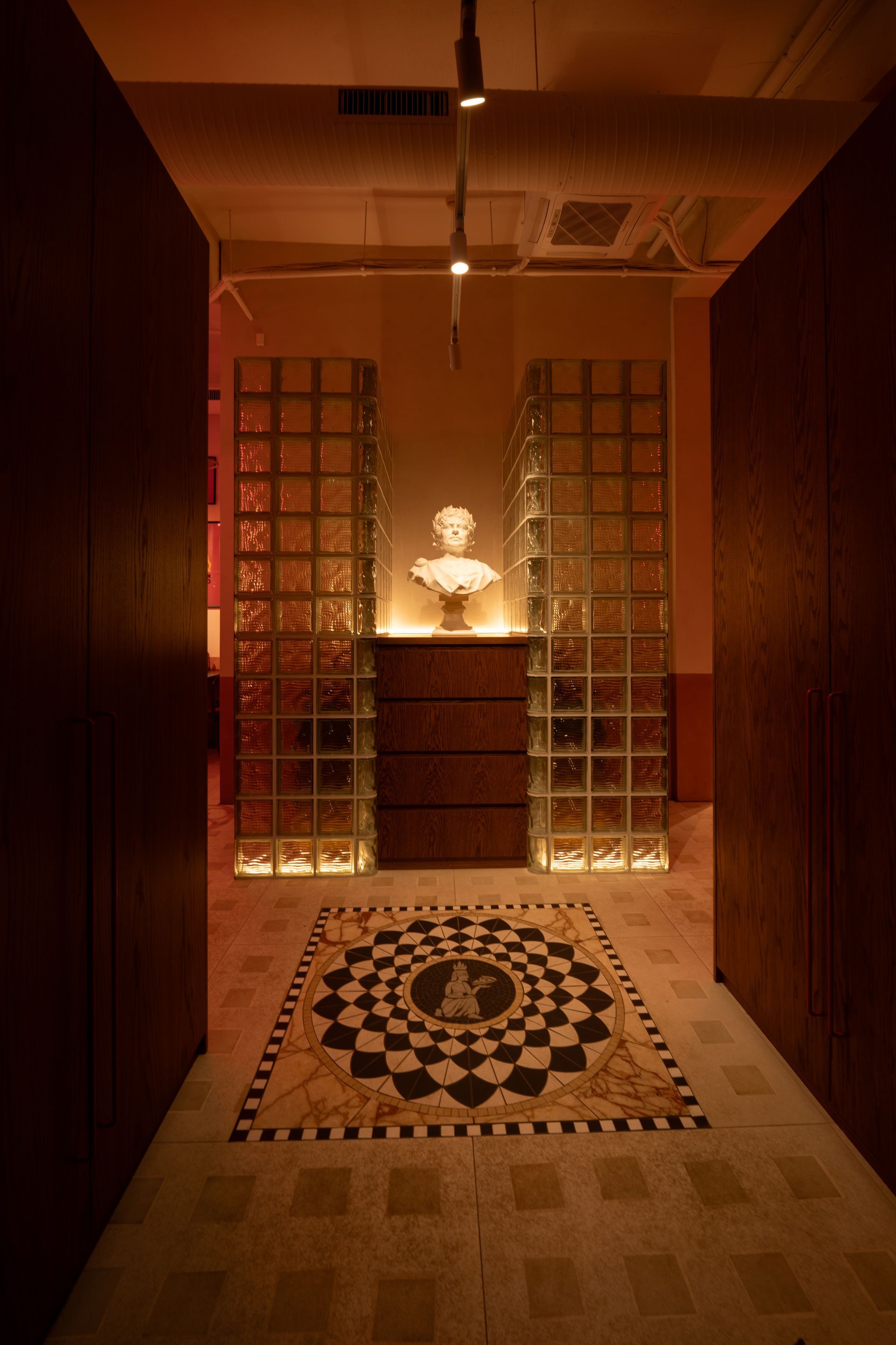 Hallway with decorative glass block walls, bust on a dresser, and patterned floor.