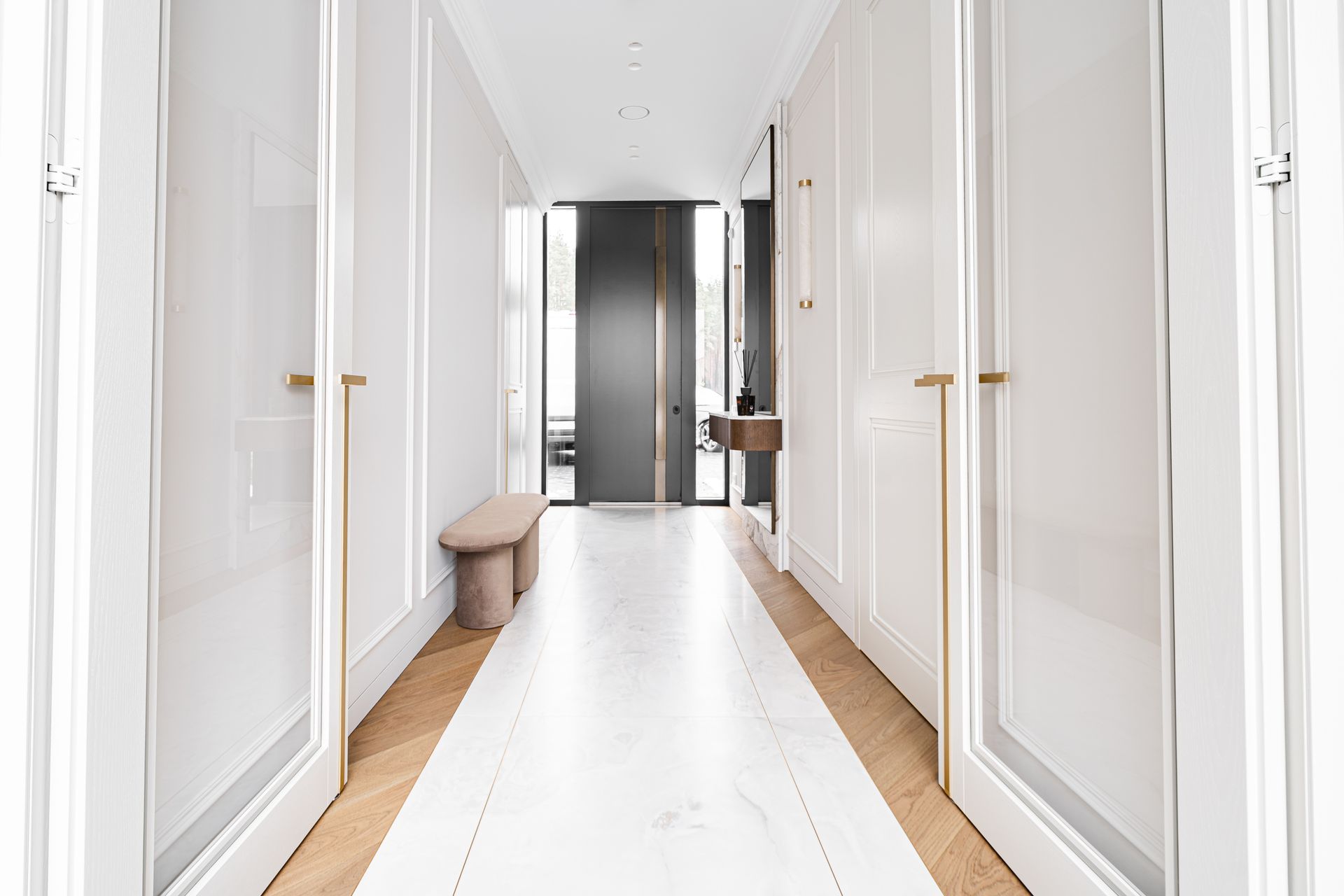 Long hallway with white walls and floor, gold door handles, and a bench.