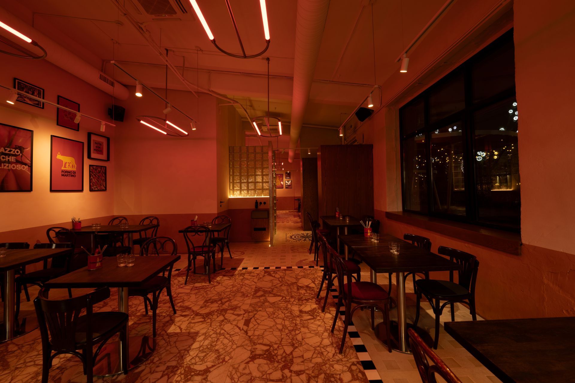 Interior view of a dimly lit restaurant with tables and chairs. Warm lighting casts an orange glow throughout the space.