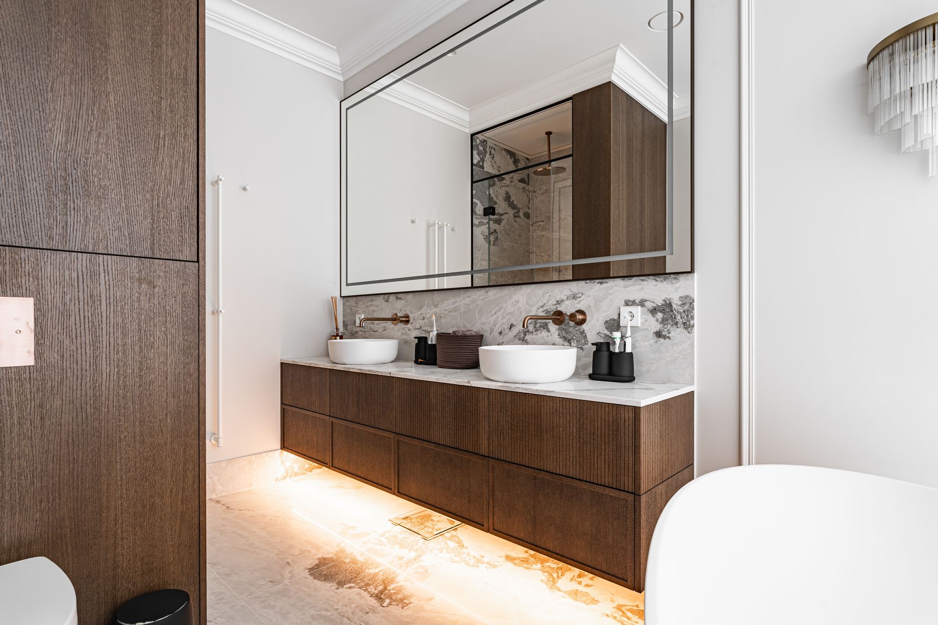 Modern bathroom with a large mirror, double sink, wood cabinets, and under-cabinet lighting.