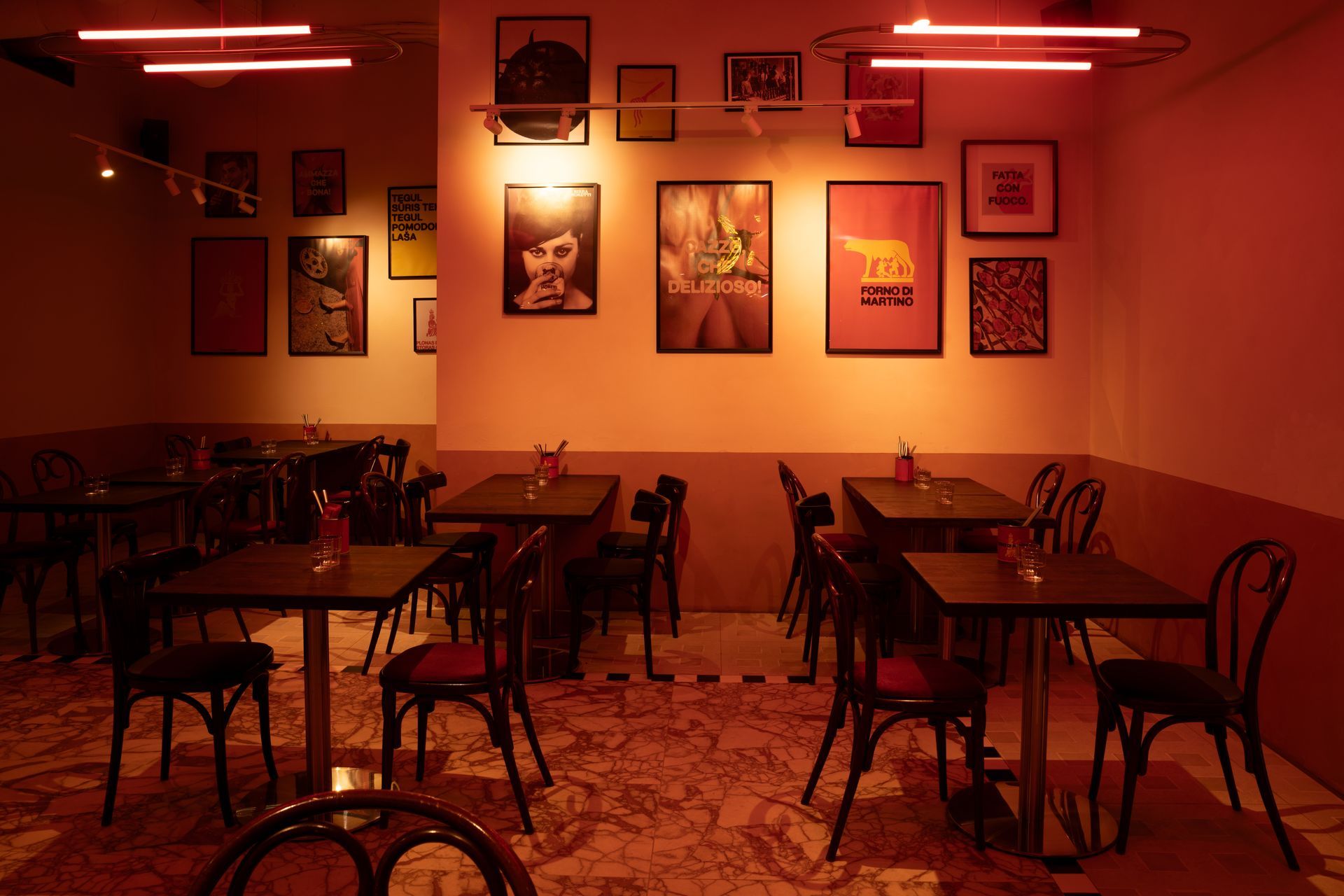 Interior of a restaurant with tables, chairs, and framed artwork on the walls; lit with red lights.