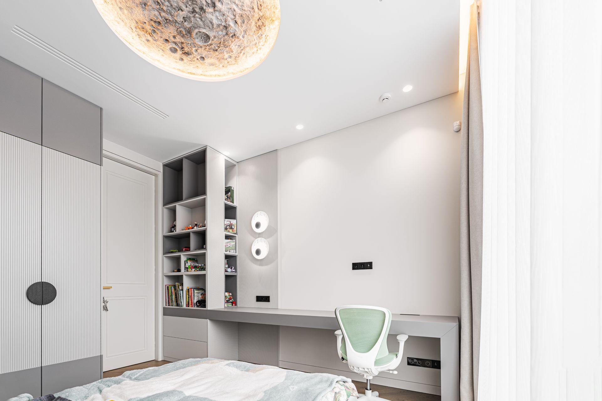 Modern bedroom with desk, built-in shelving, white walls, gray accents, and a spherical ceiling light.