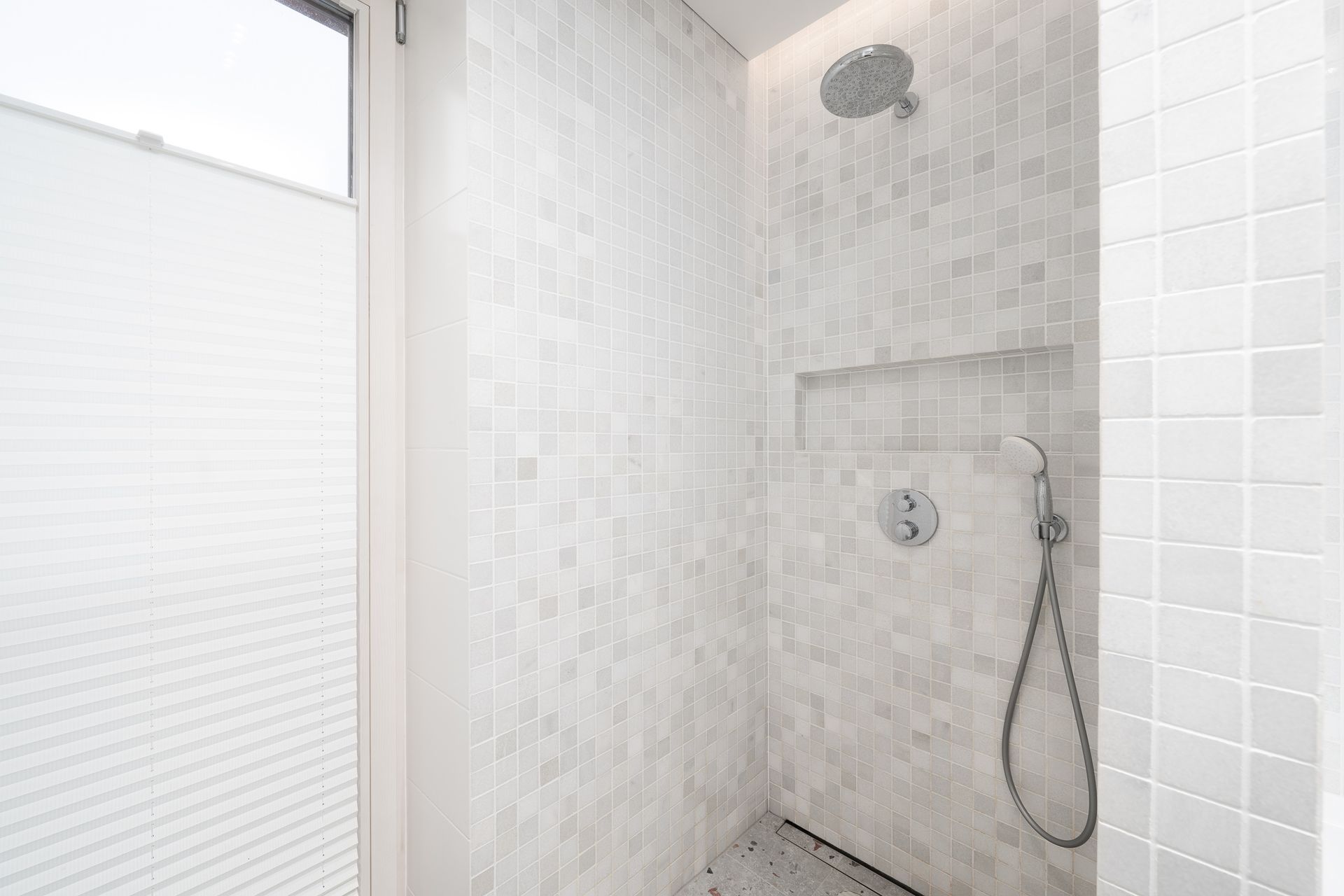 Dušas vonios kambaryje su baltomis plytelėmis ir langu.