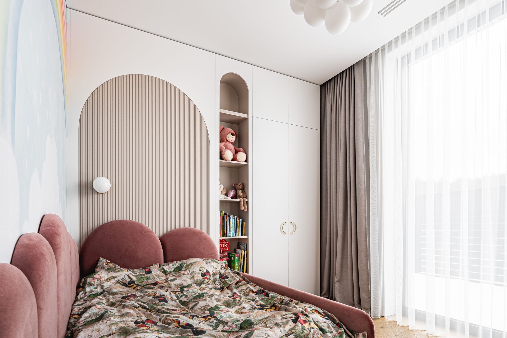 Pink-themed child's bedroom with bed, built-in storage, and tall window with sheer curtain.