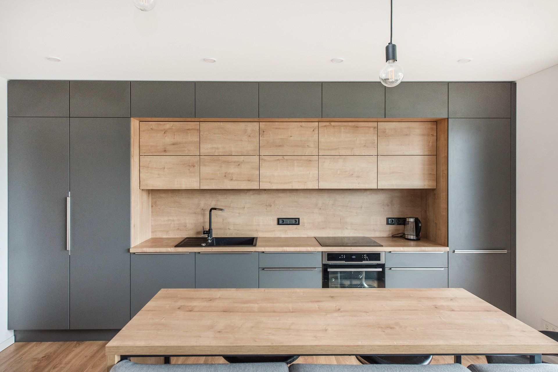 Virtuvė su medinėmis spintelėmis ir mediniu stalu.