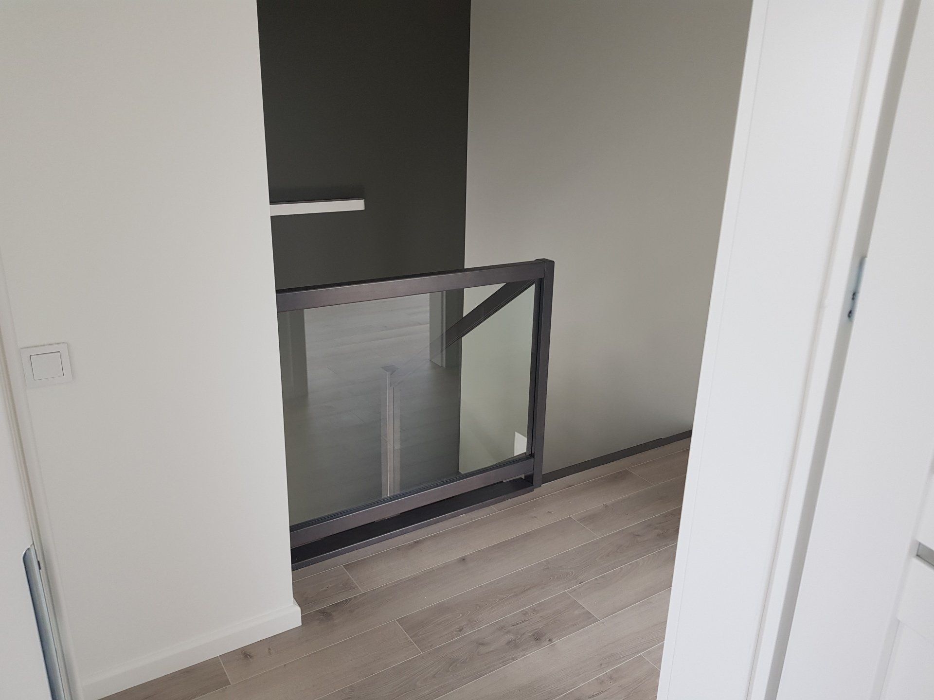 Durų anga, vedanti į laiptus su stikliniais turėklais.