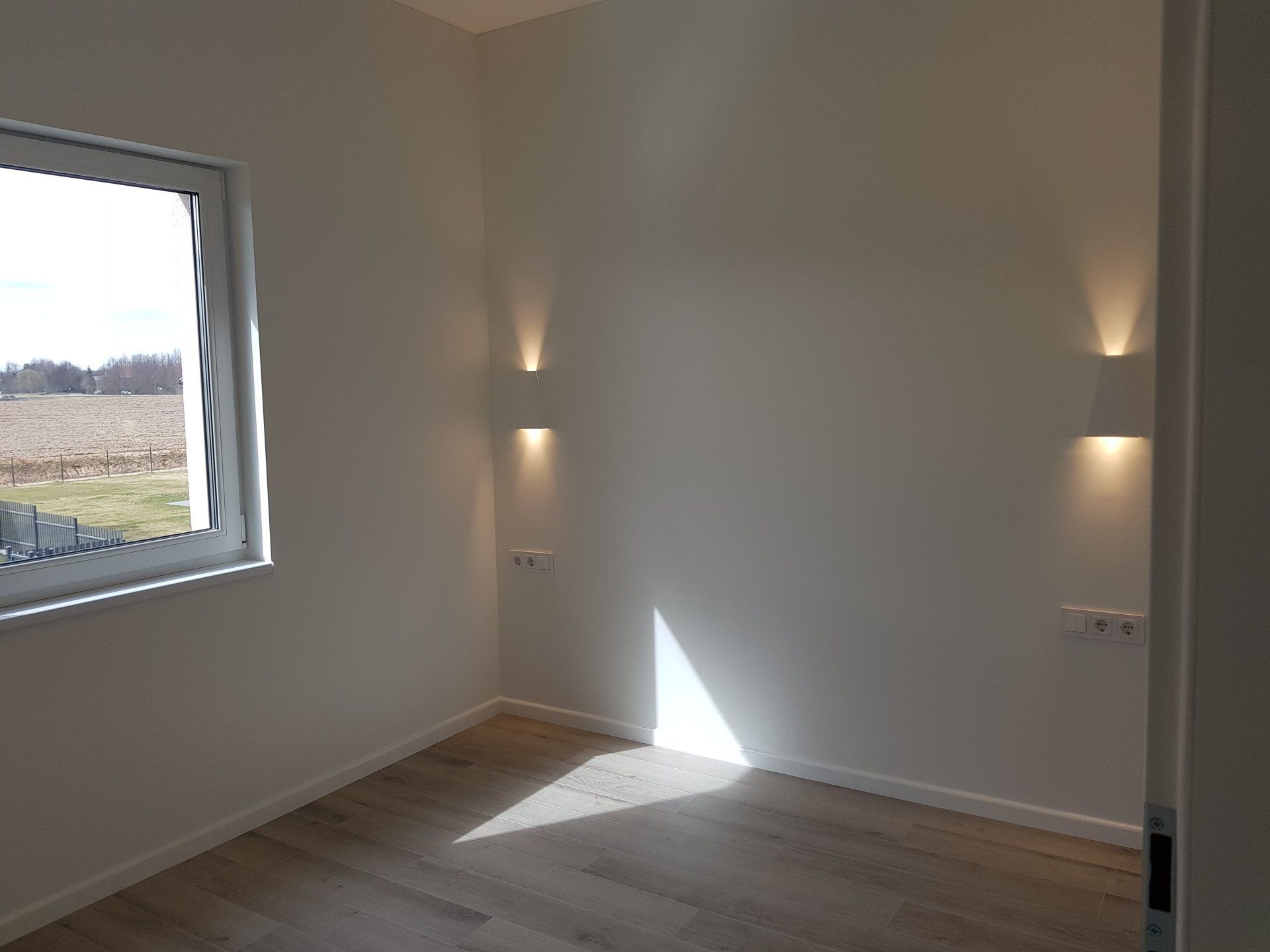 Tuščias kambarys su langu ir lempute ant sienos.